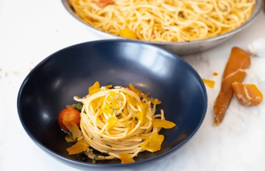 Assiette de spaghetti aux copeaux de boutargue, tomates confites et tranches de boutargue posées à côté.